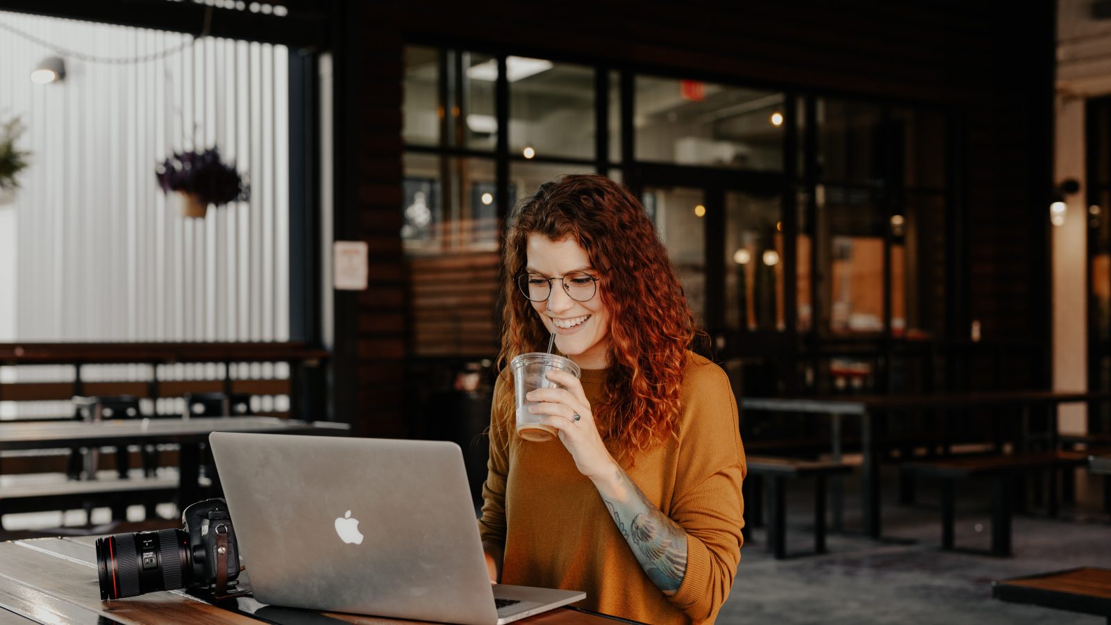 woman in brown long sleeve shirt sitting by the table using macbook