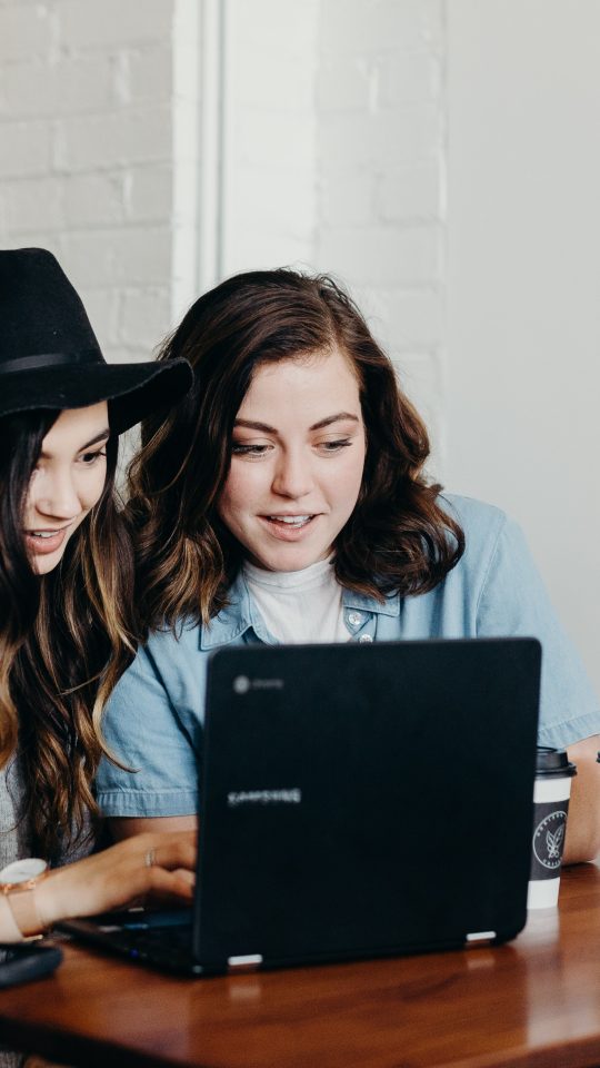 two woman sitting near table using Samsung laptop